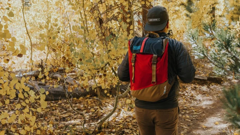 Person walking through autumn woods wearing a red and tan Mafia recycled-sail backpack